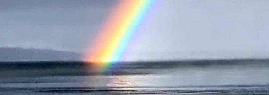 orange yellow blue purple rainbow over a serene ocean